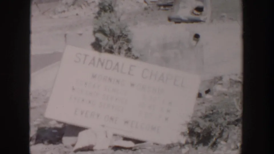Grand Rapids home-movie frame of the Standale Chapel sign listing services while tilted among debris in 1956.