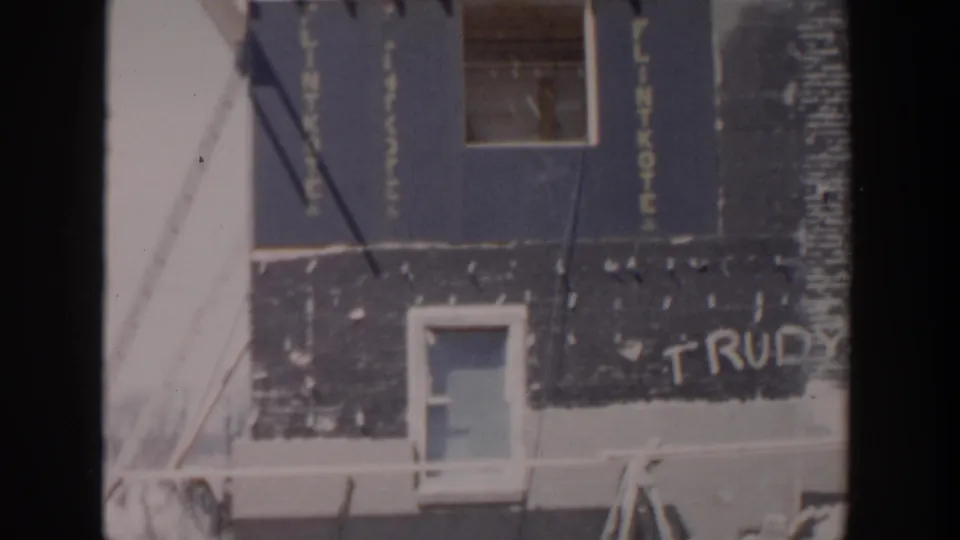 1956 Grand Rapids frame of an unfinished house facade with tarpaper siding, windows, overhead lines, and partially visible TRUDY graffiti.