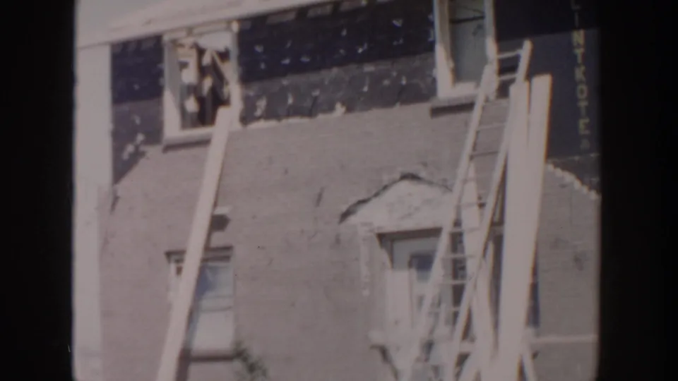 1956 Grand Rapids construction frame with a ladder, leaning boards, upper window area, and unfinished exterior surfaces on a residential building.