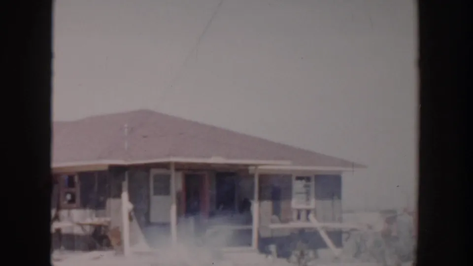 1956 Grand Rapids home construction view showing a low-roofed single-story house, porch area, open doorway, and hazy foreground.