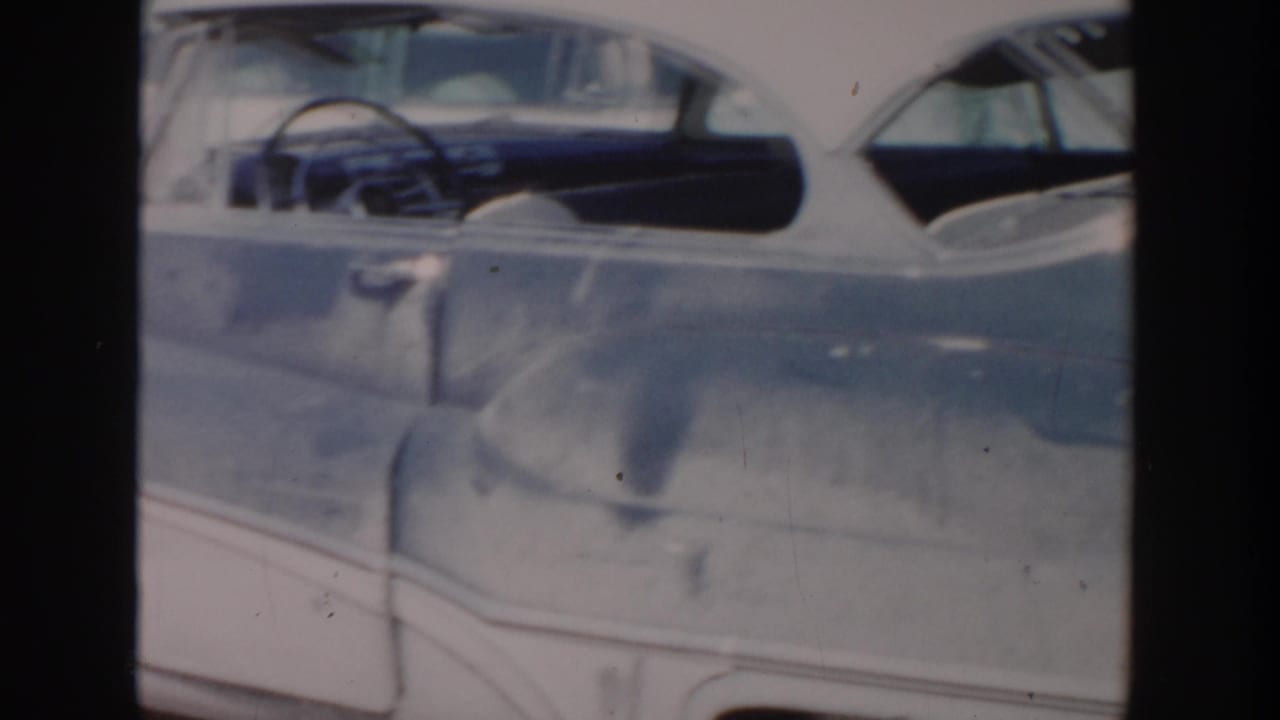 1956 Grand Rapids home-movie frame showing a damaged grey car body with its side windows and steering wheel visible.