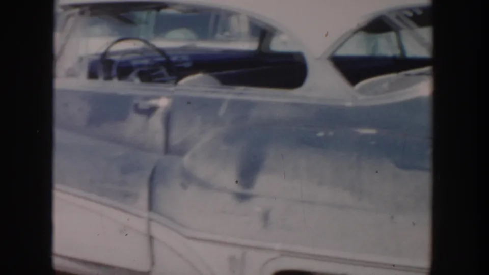 1956 Grand Rapids home-movie frame showing a damaged grey car body with its side windows and steering wheel visible.
