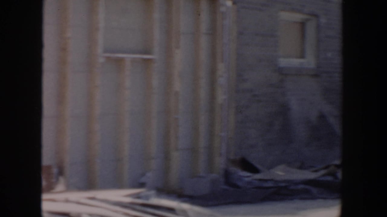 Exterior wall of a house under construction with window opening and material on the ground.