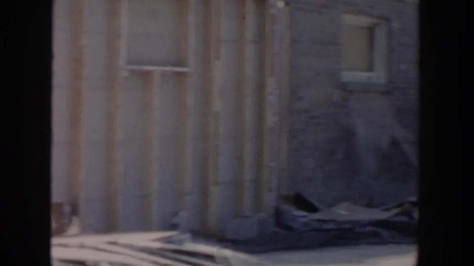 1956 Grand Rapids frame showing a house exterior under construction, with block wall, window opening, and debris or materials nearby.