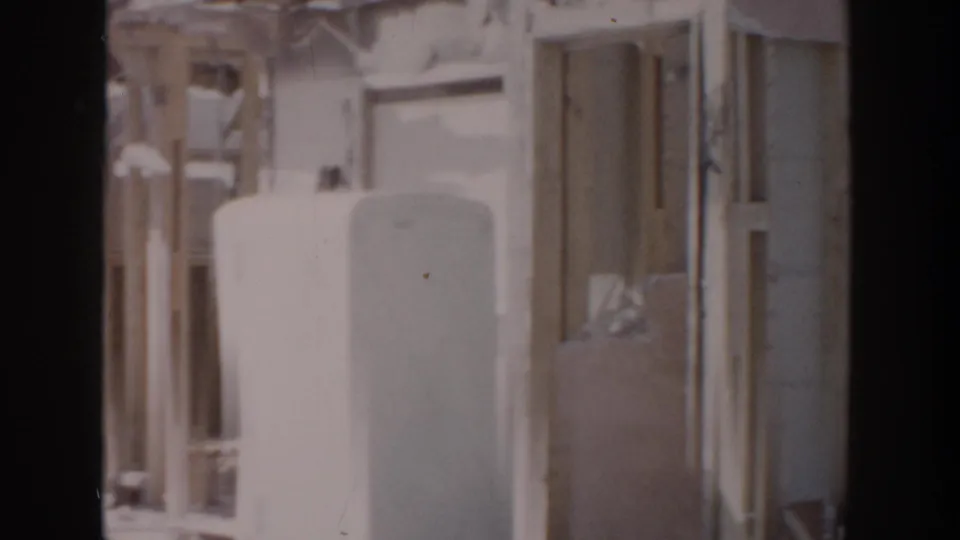 1956 Grand Rapids home-movie frame showing exposed house framing, a large tank, and unfinished door and window openings.