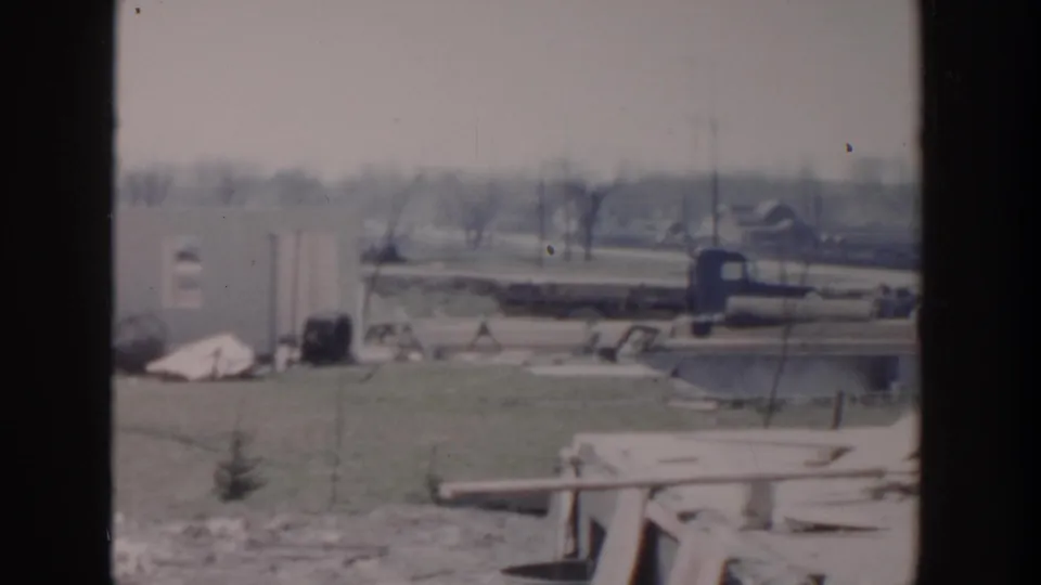 1956 Grand Rapids worksite view with a blue pickup truck, open grass, utility poles, and roadside construction materials.