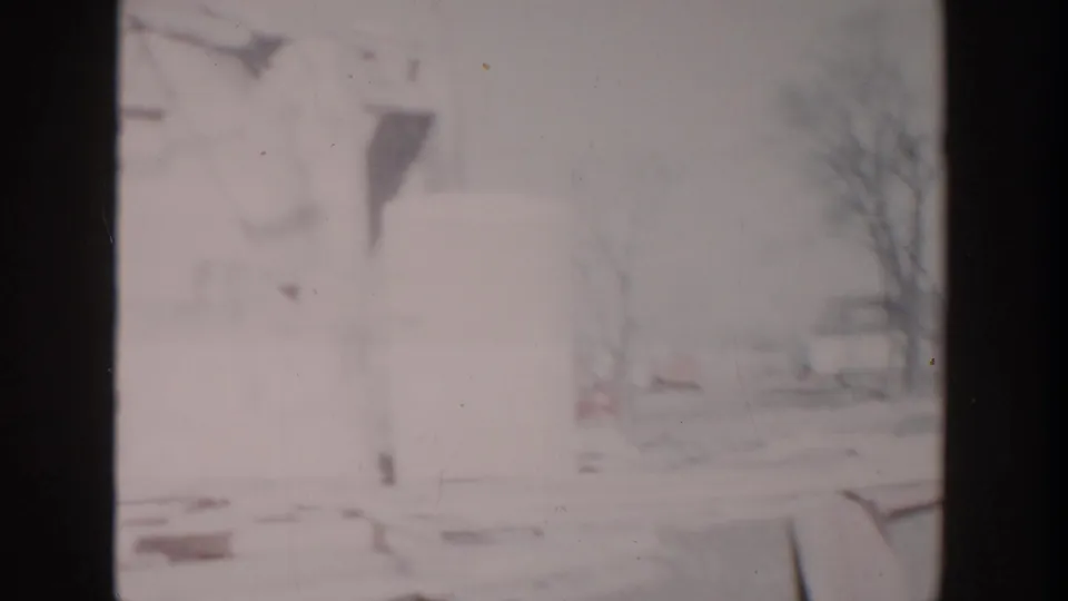 Faded 8mm frame from the Grand Rapids site showing pale building panels, a tree, road edge, and loose lumber.