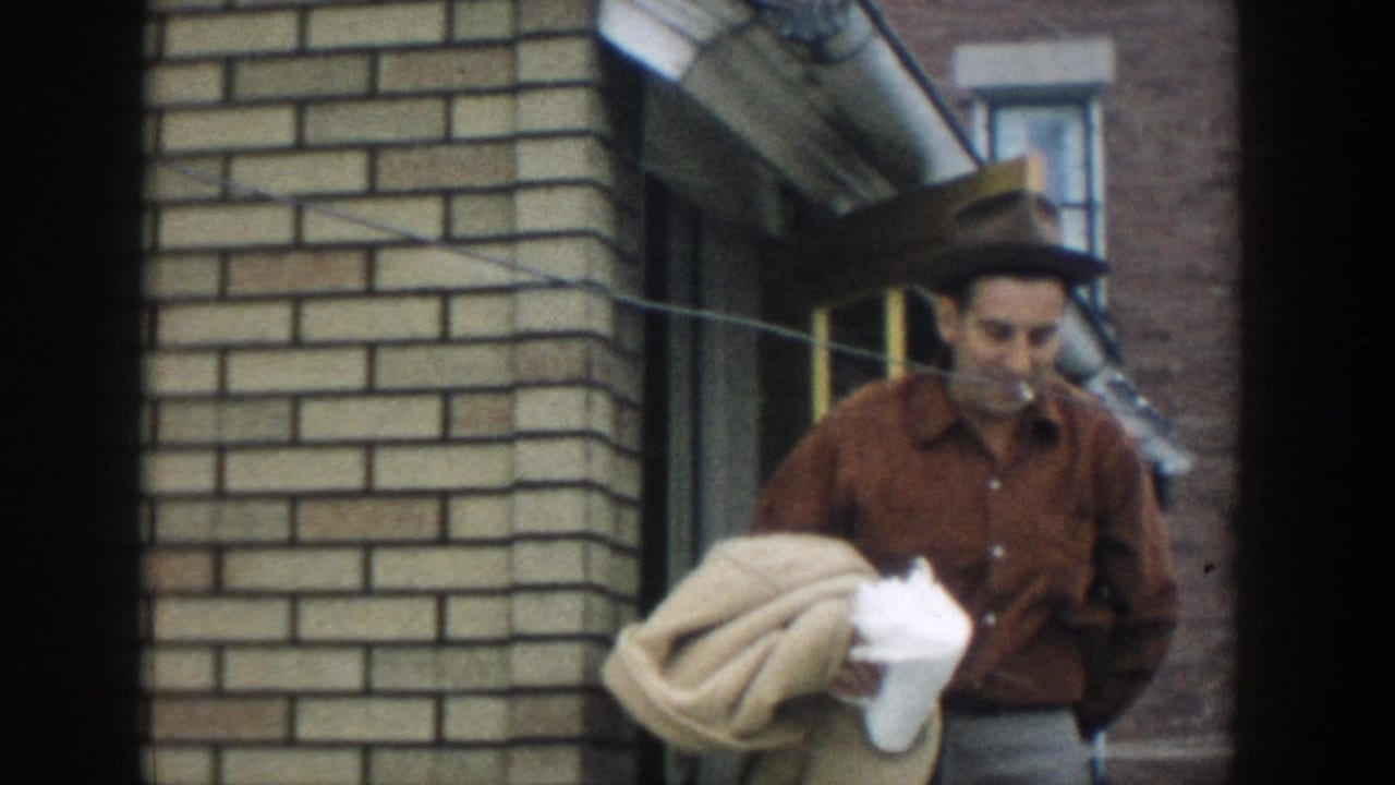 The man appears at the doorway with a cigarette, holding bundled fabric against a brick building exterior in Michigan, 1957.