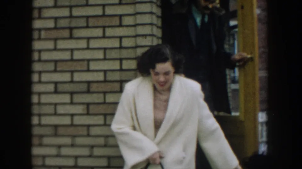 The woman descends from the brick entrance with her handbag, with a second adult partly visible in the doorway behind her.