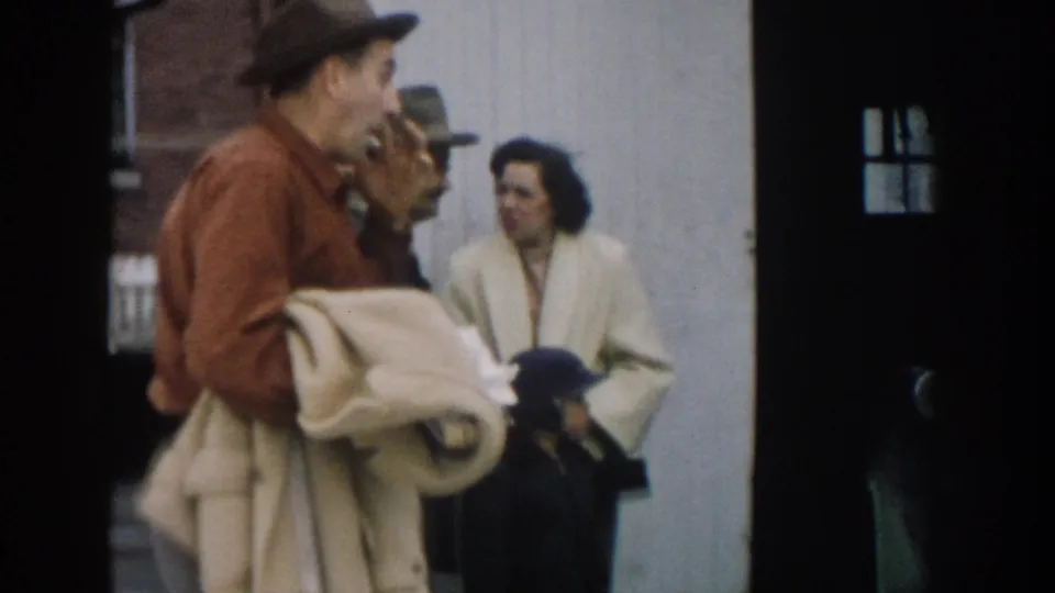 In the closing frame, a man carries a folded coat as adults talk nearby and a small dark dog appears at the lower edge.