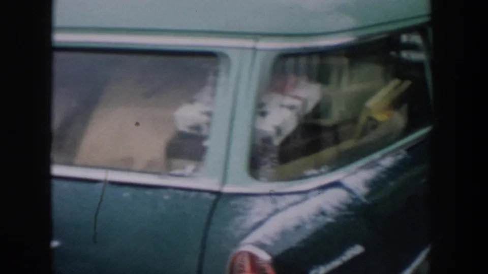 The green station wagon fills the frame, showing its side windows and rear light while a person is partly visible at the right edge.