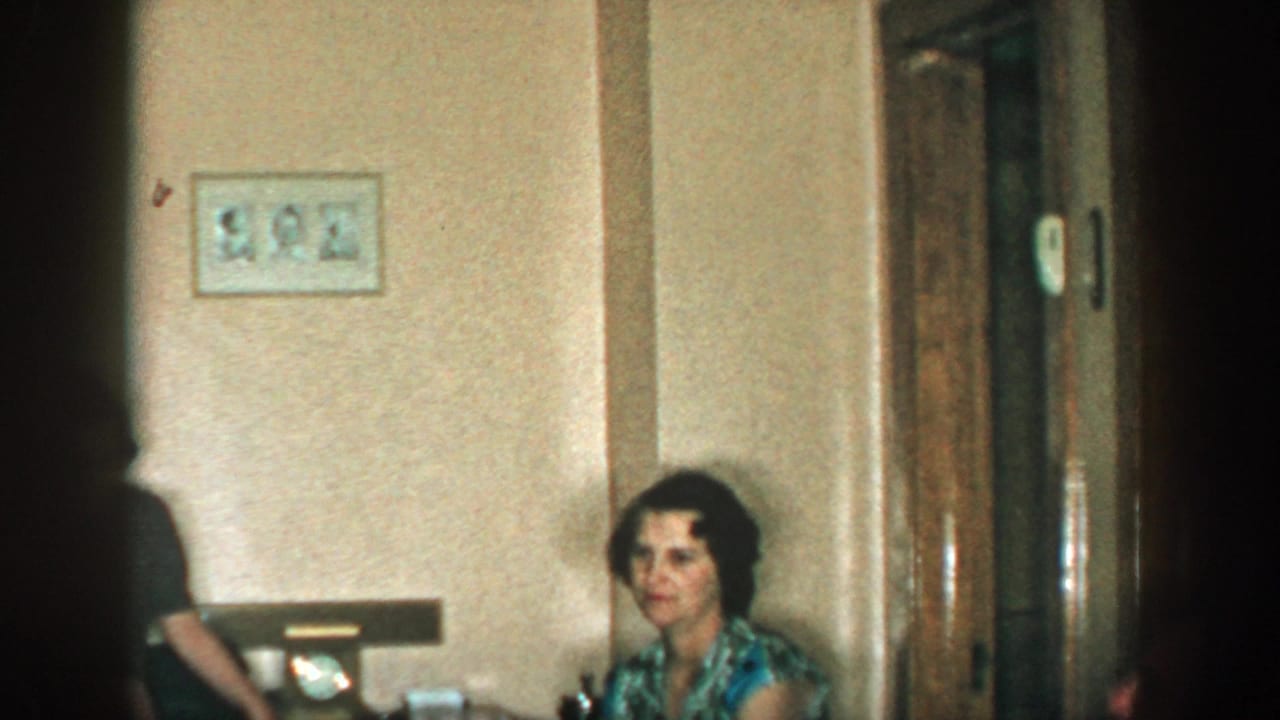 A seated woman appears near wood doors while another person is partly visible in the center.