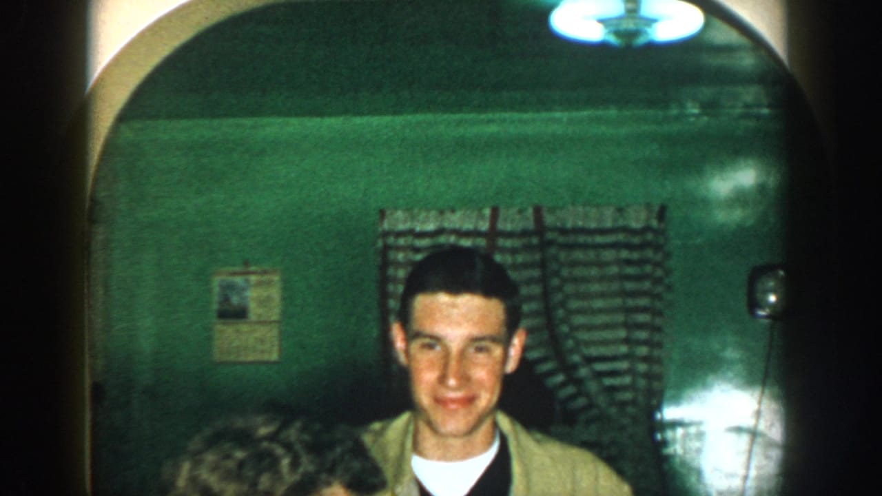 Young man facing the camera in the same green room, partially cropped by the lower frame edge.