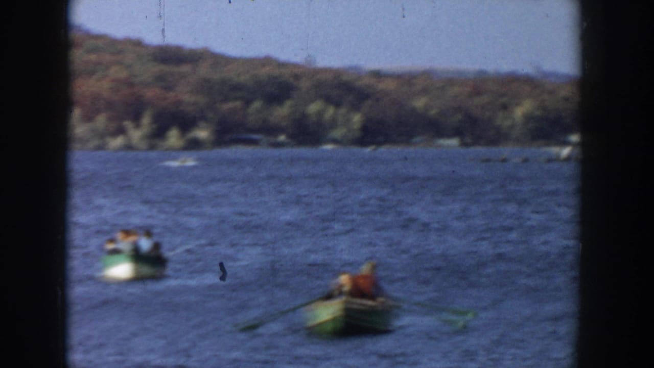 Two small rowboats on a lake with wooded shoreline behind them.