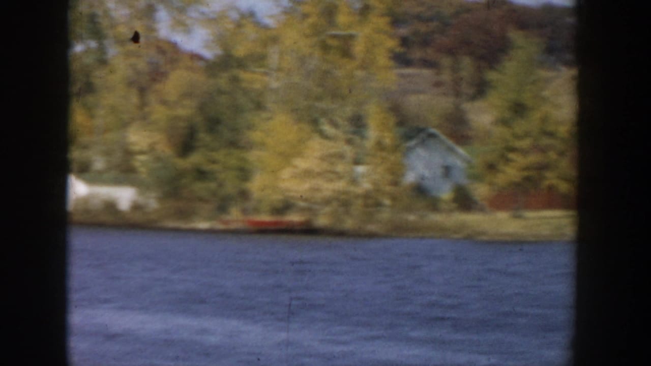 1957 Wisconsin lake footage showing a small lakeside house or cabin among autumn trees, with water in the foreground.