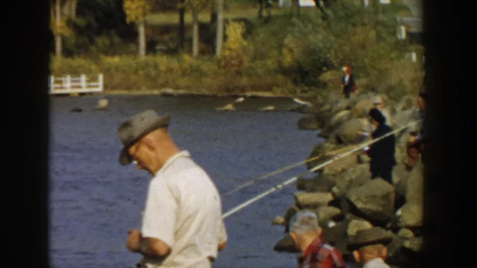1957 Wisconsin lakeshore scene with anglers positioned on rocks and a man in a hat prominent in front.