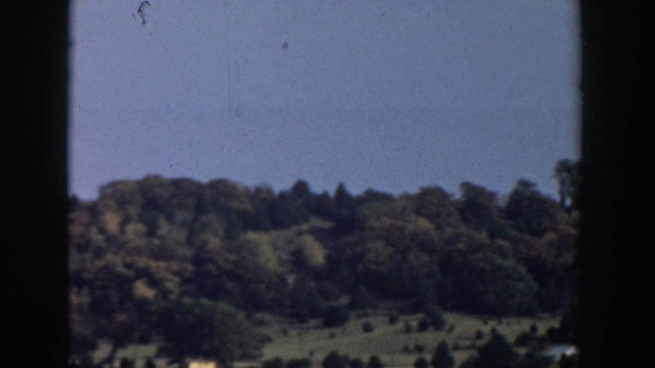 1957 Wisconsin landscape view through a moving vehicle window, with wooded hills and open slopes in the distance.