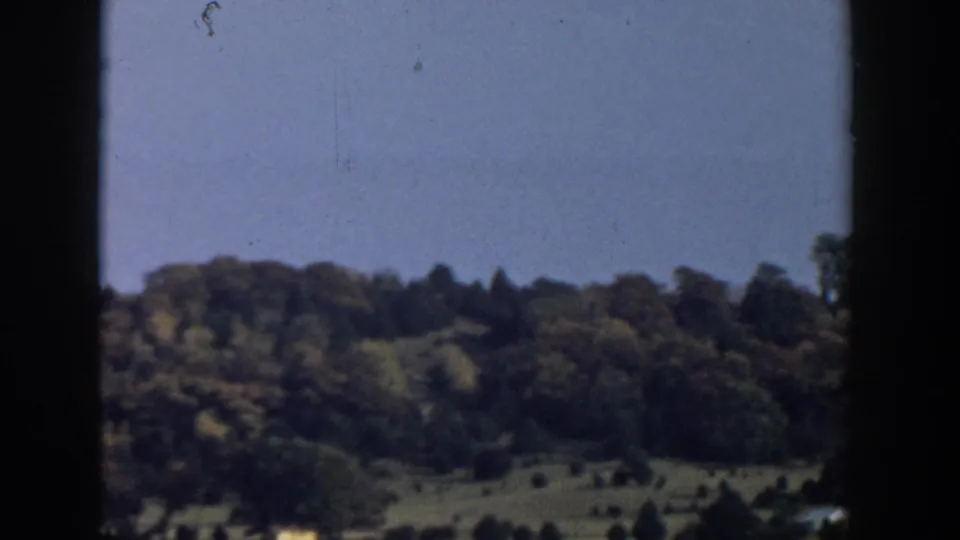1957 Wisconsin landscape view through a moving vehicle window, with wooded hills and open slopes in the distance.