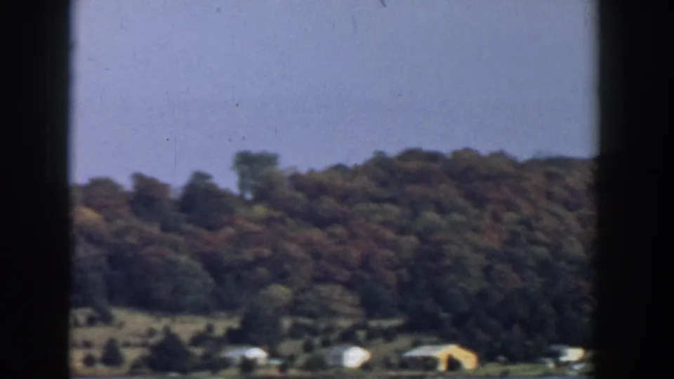 1957 Wisconsin rural hillside with dense trees, open ground, and small houses visible below.