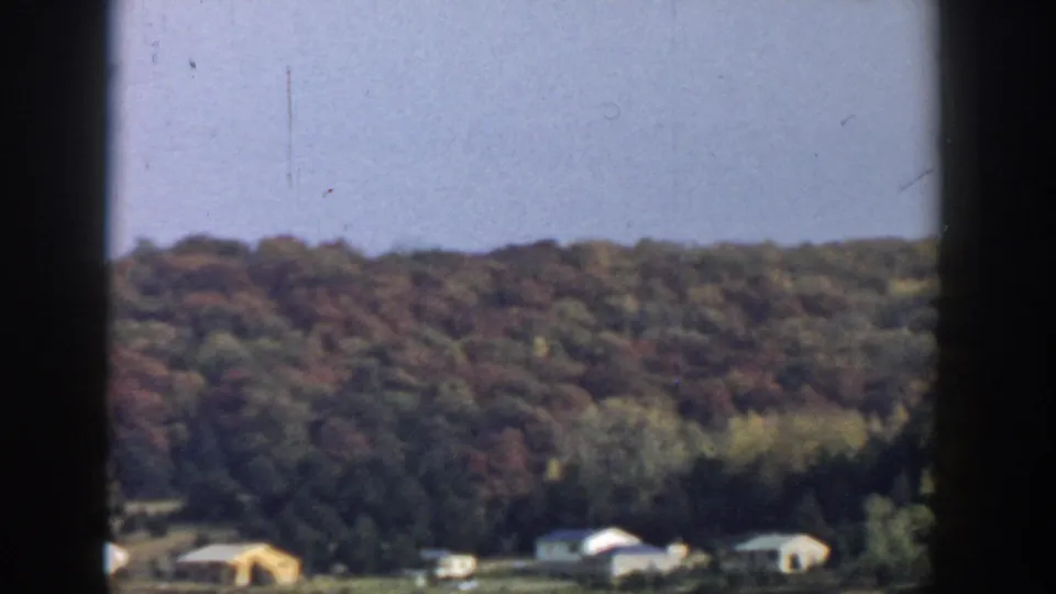 1957 Wisconsin home-movie view of scattered houses at the base of a tree-covered hillside.