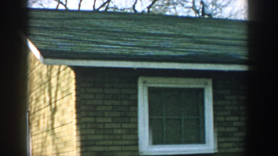 1957 Wisconsin frame showing a quiet brick residential exterior with a centered white-trimmed window and leafless trees above the roofline.