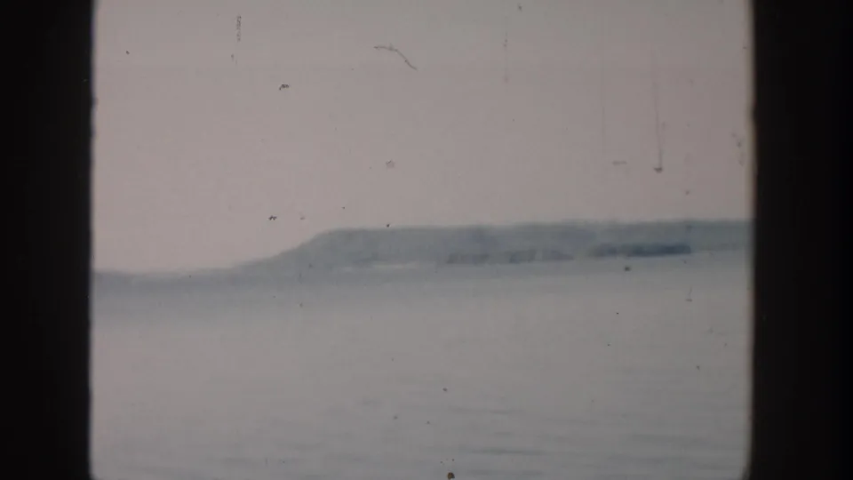 1957 Wisconsin 8mm frame showing still lake water and distant rolling hills through a dark window-like frame.