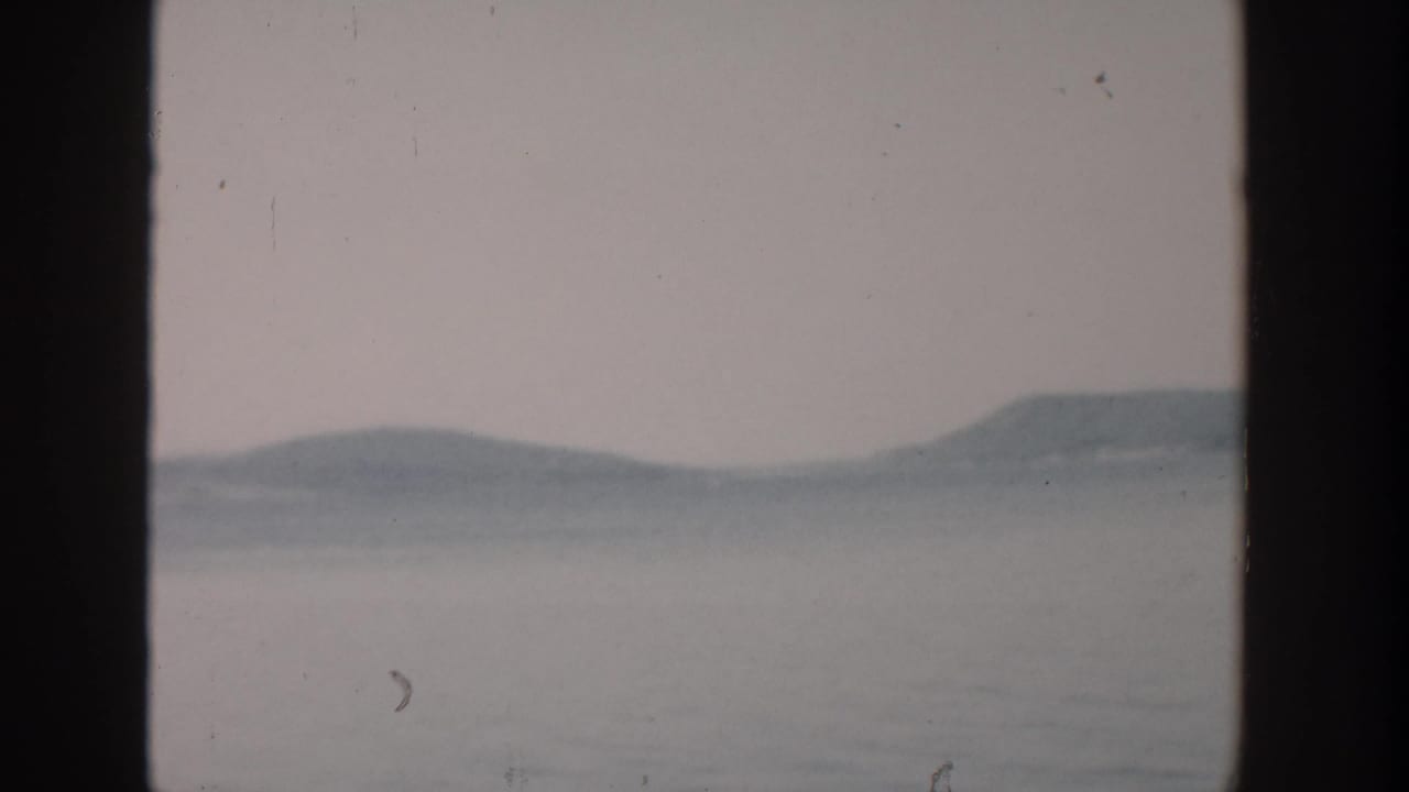 Wide still lake under a pale sky with distant hills and dark vertical borders.