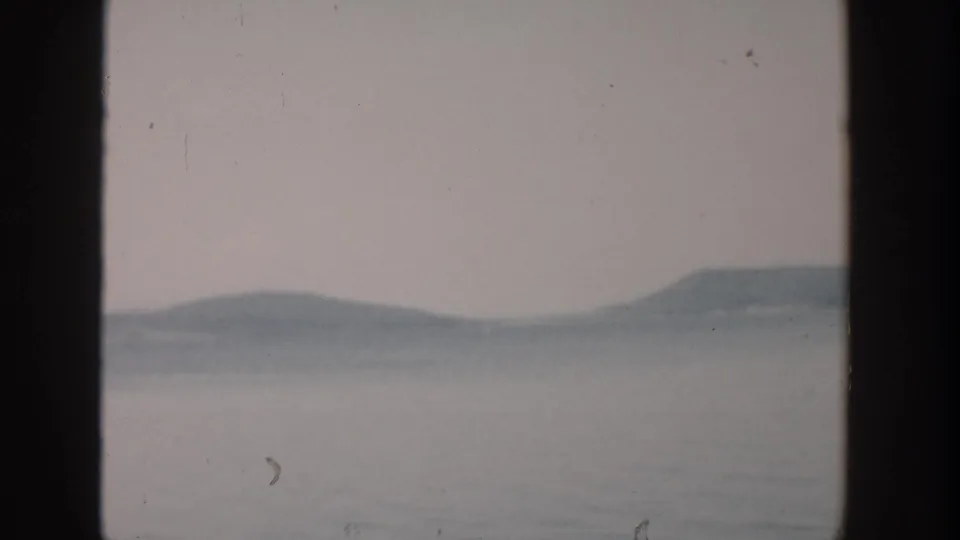 1957 Wisconsin home-movie view of calm lake water and hazy hills framed by dark vertical edges.