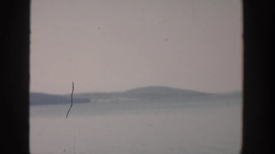 1957 Wisconsin 8mm still showing hazy lake water, low shoreline hills, and visible film scratches.