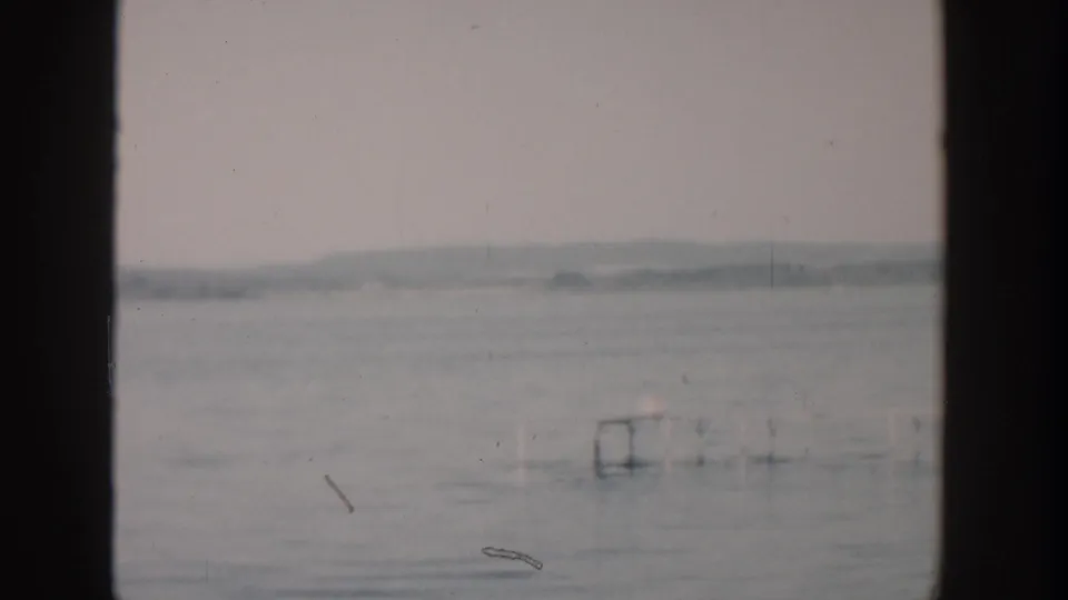 1957 Wisconsin 8mm frame showing calm water, hazy land in the distance, and dark borders from the filmed viewpoint.