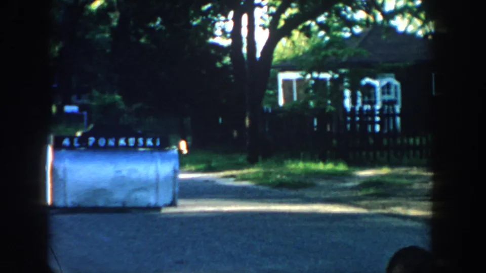 1957 Wisconsin frame showing AL PONKUSKI lettering on a white machine near a shaded residential street and house.