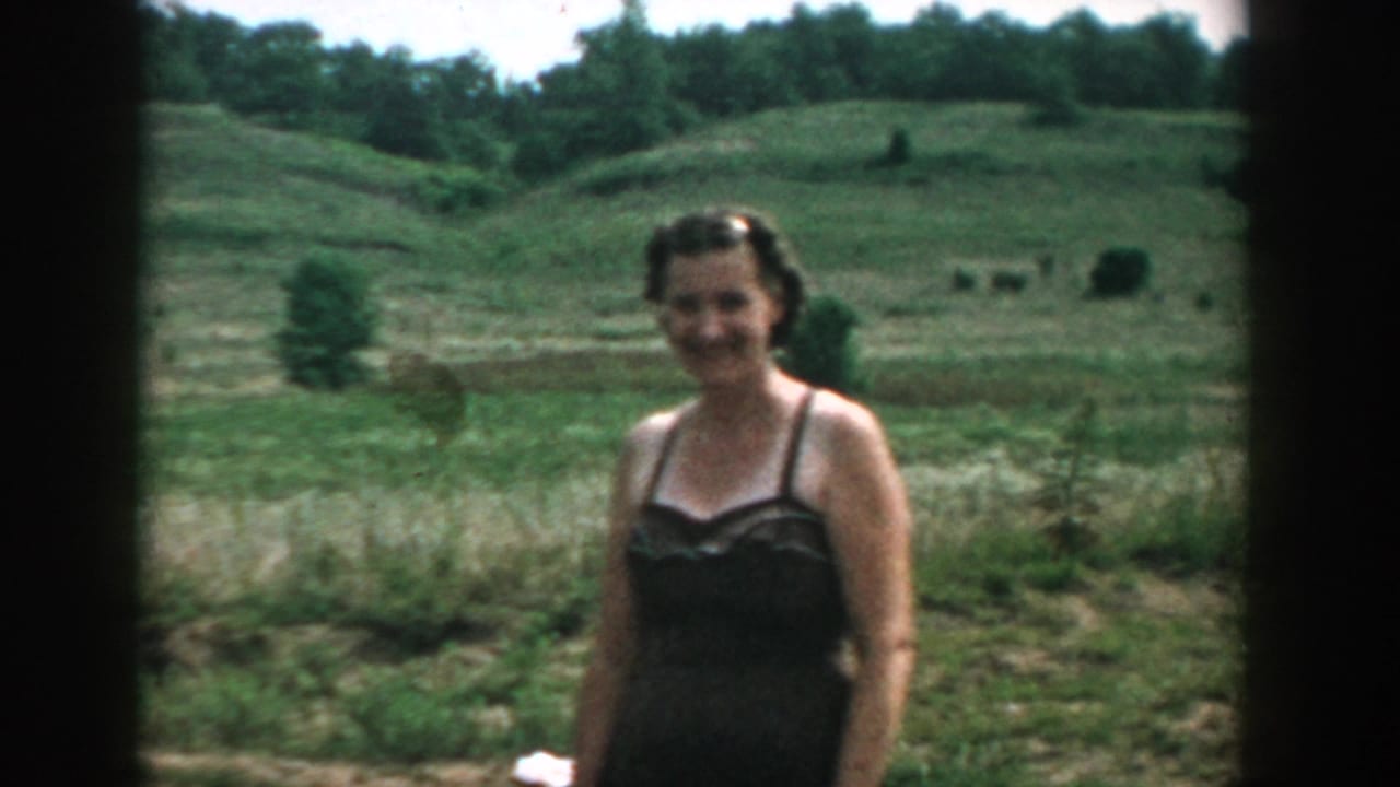 Woman in a dark swimsuit standing in front of open grassland and trees.