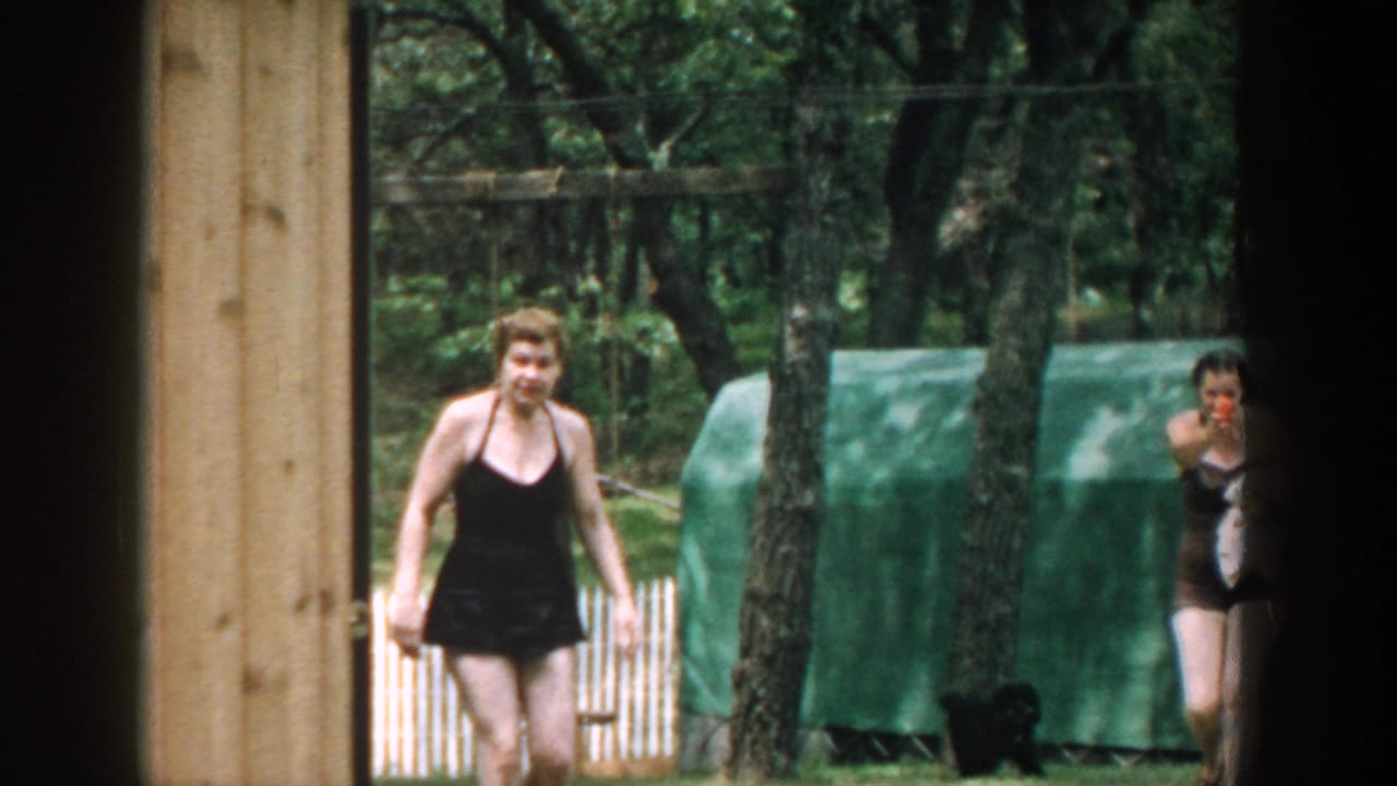 Woman in a black bathing suit walking outside near trees and a green covered structure.
