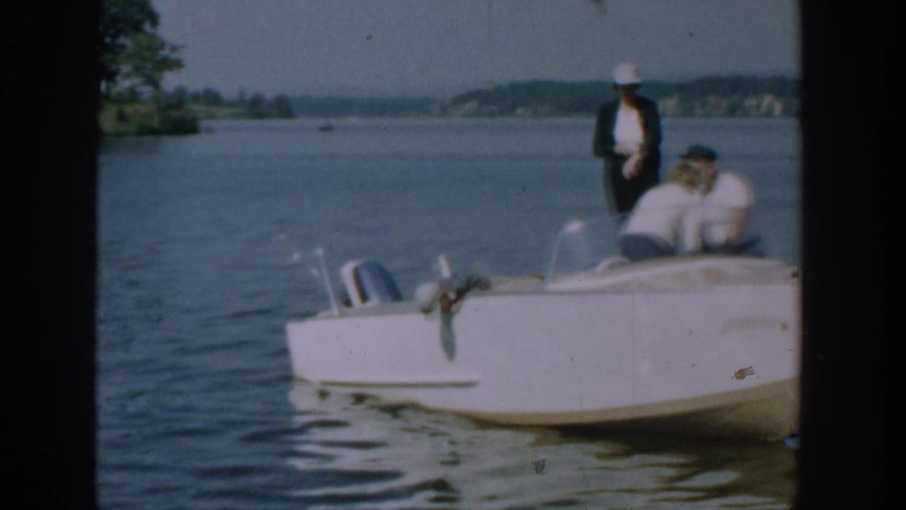 Three adults on a white motorboat beside calm lake water near a dock.