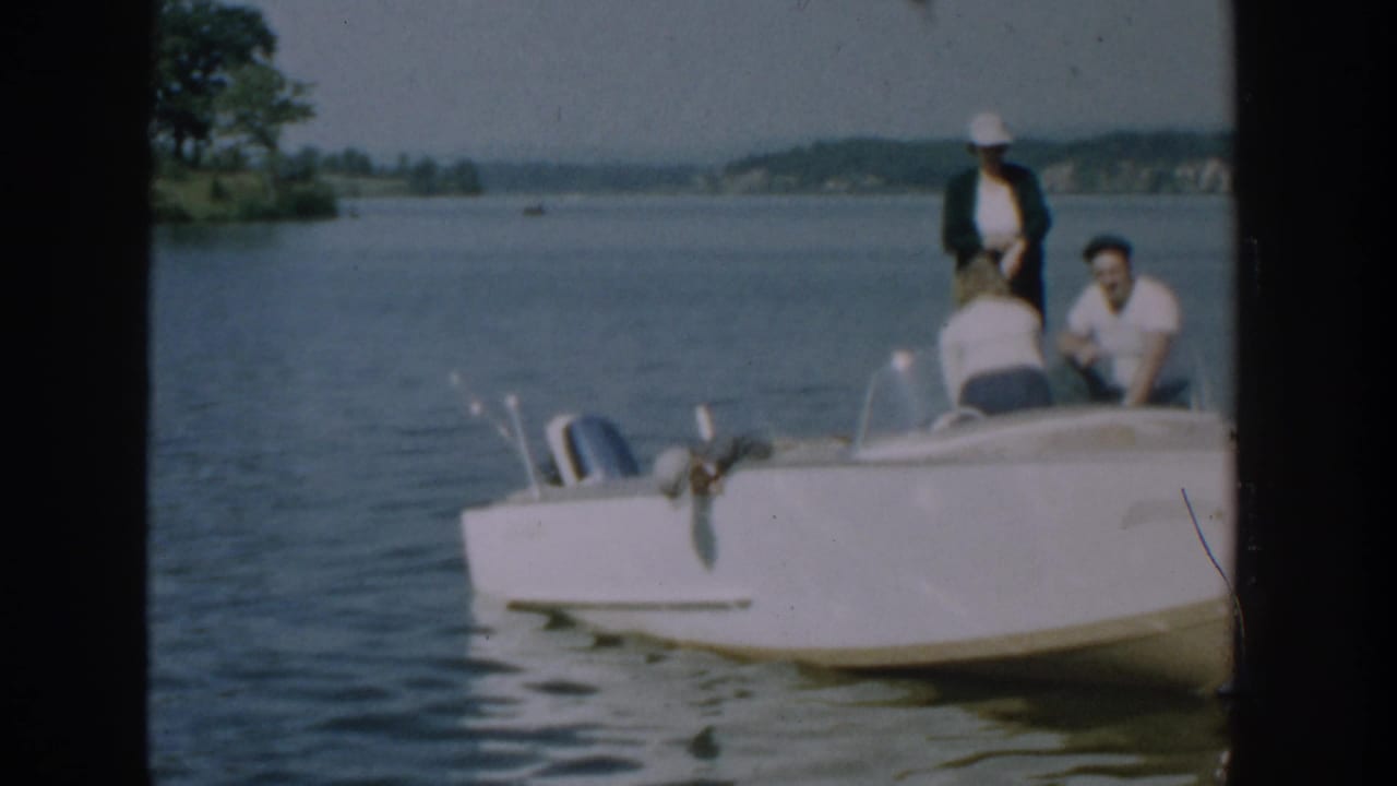 Adults gather near the bow and stern of a white motorboat on a lake.