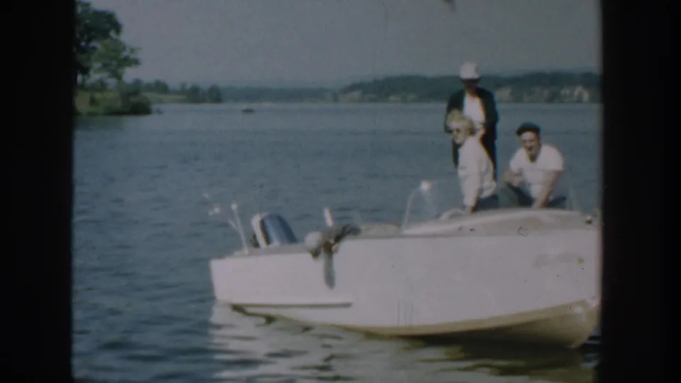 1957 Wisconsin lake footage shows a woman and two men aboard a white motorboat near the dock, with shoreline beyond.