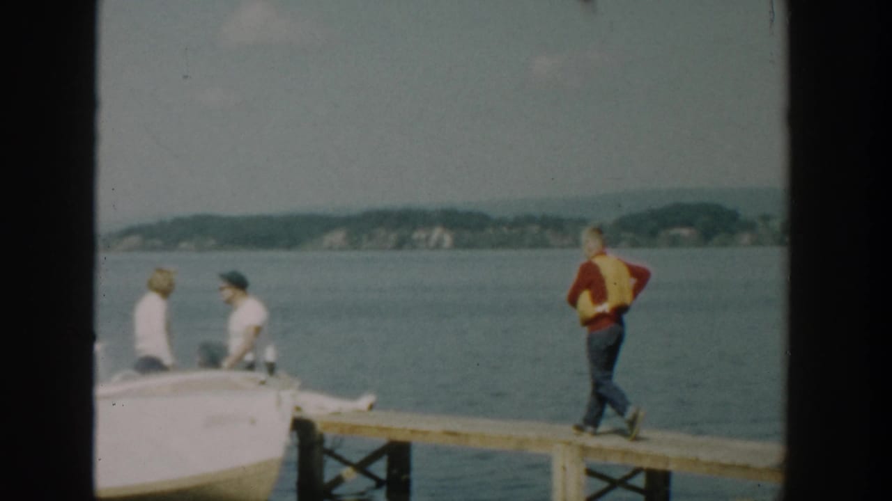 Small white motorboat reaches the dock while a man in a life vest waits.