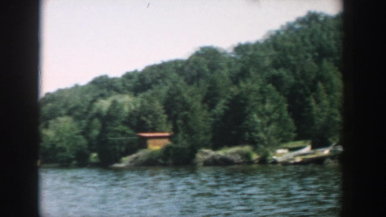 Calm river seen from a boat with wooded shoreline and a small waterside structure.