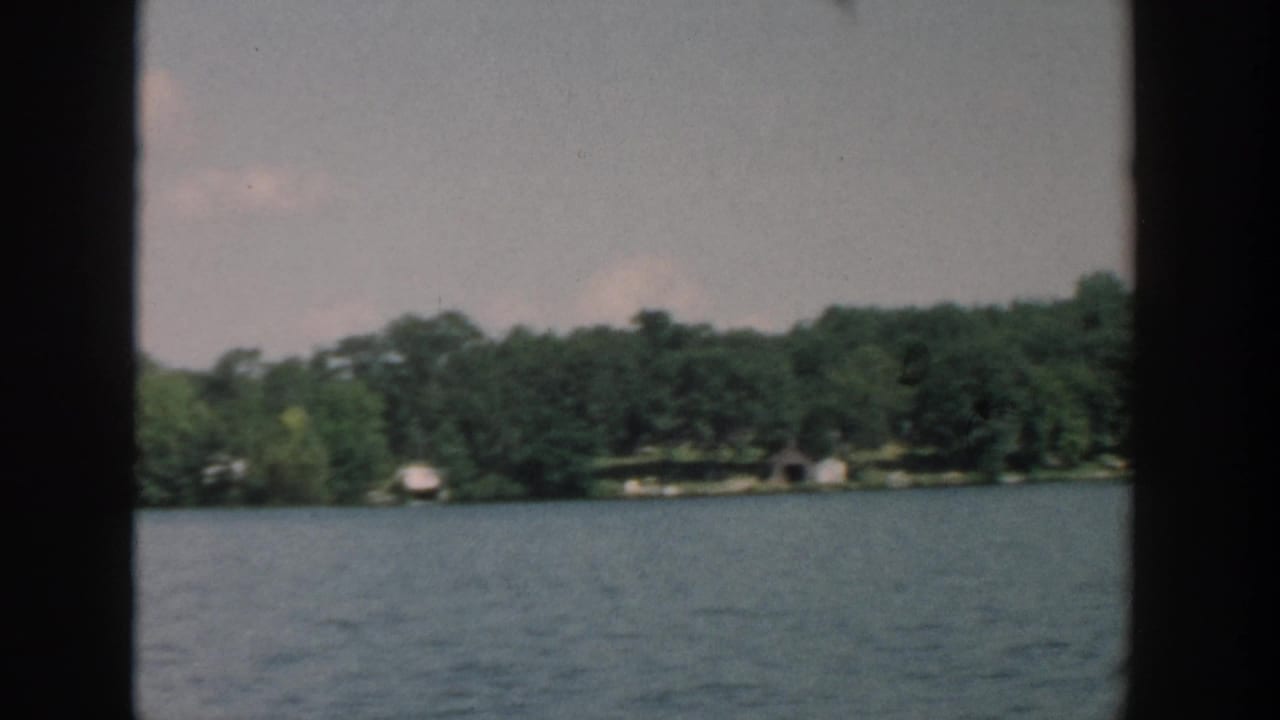 Lake water with a tree-lined shoreline and small pale structures in the distance.