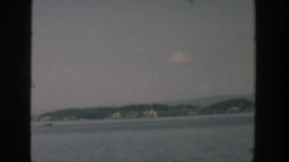 1957 Wisconsin 8mm frame showing a broad lake surface and distant low shoreline bluffs under a muted sky.