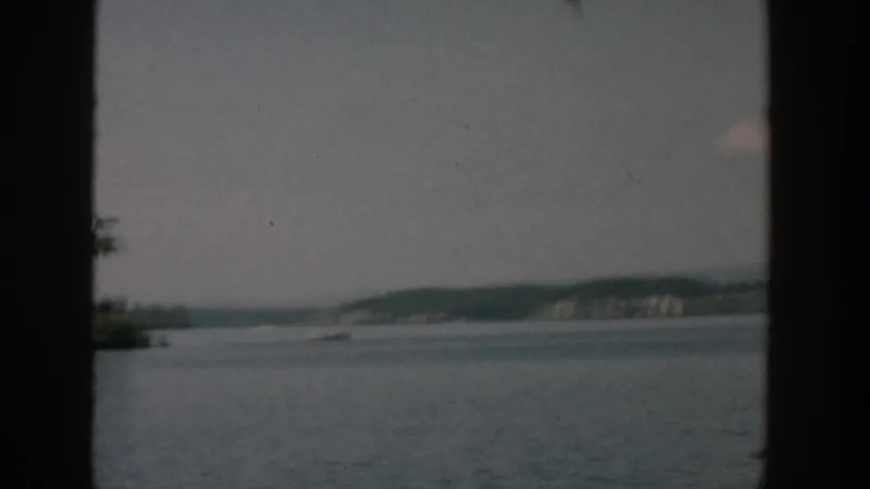 1957 Wisconsin lake scene with open water, a distant tree-lined shore, and a small wooded point at the frame edge.