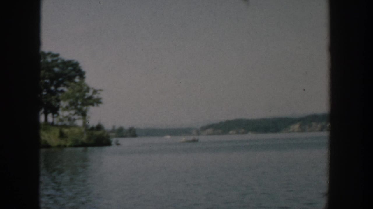 Small tree-covered island across calm lake water with distant shoreline and dark frame borders.