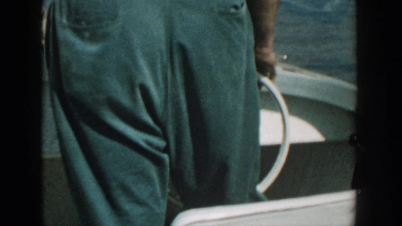 Close view of green trousers beside a white boat railing on the water.