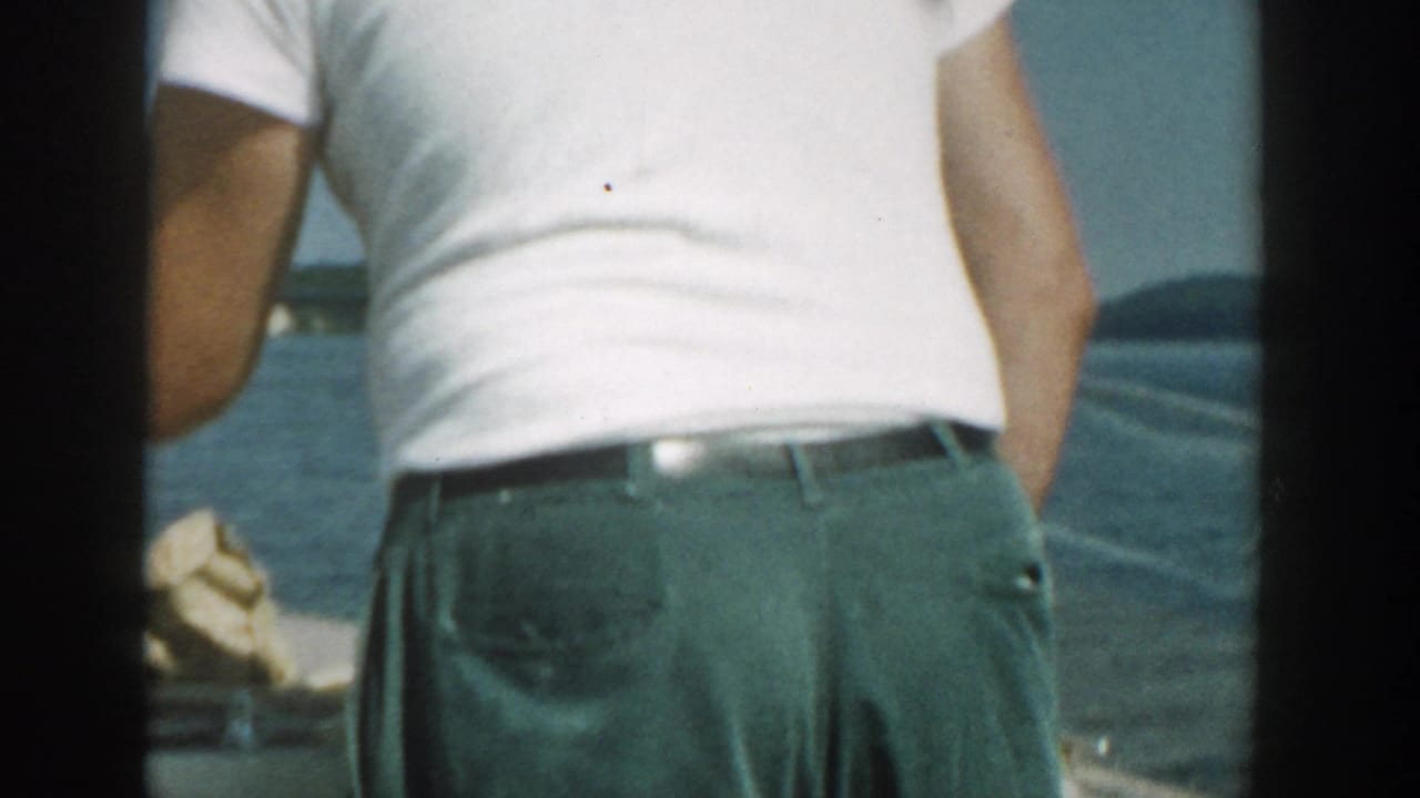 Adult man in a white t-shirt and green trousers standing on a motorboat.