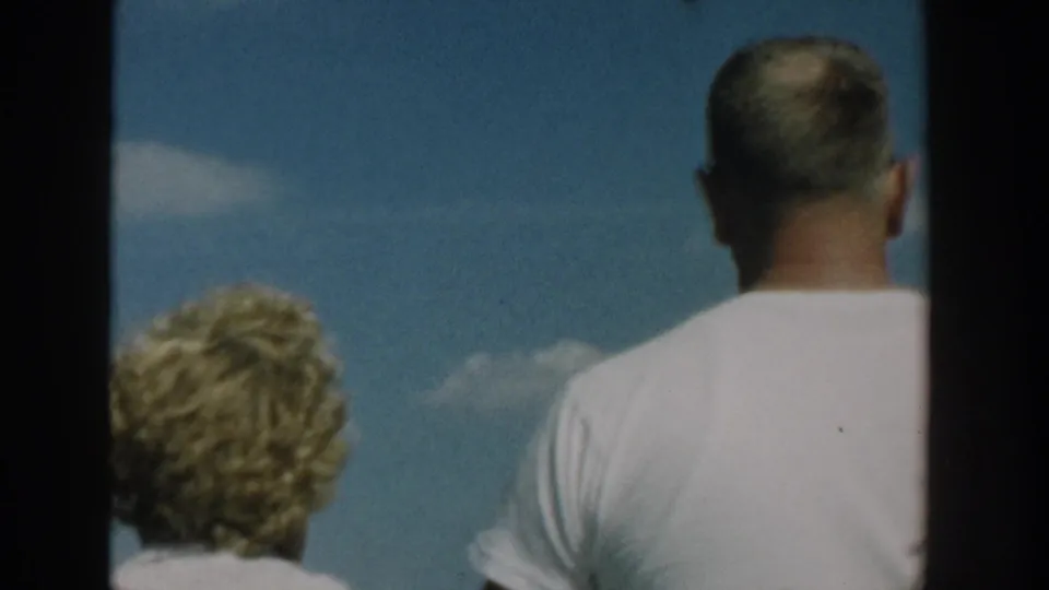 Adult man and blonde woman seen from behind aboard a motorboat in Wisconsin, 1957, with blue sky and soft 8mm film texture.