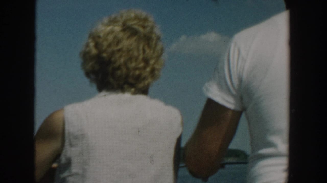 Two adults seen from behind on a boat under a blue sky.