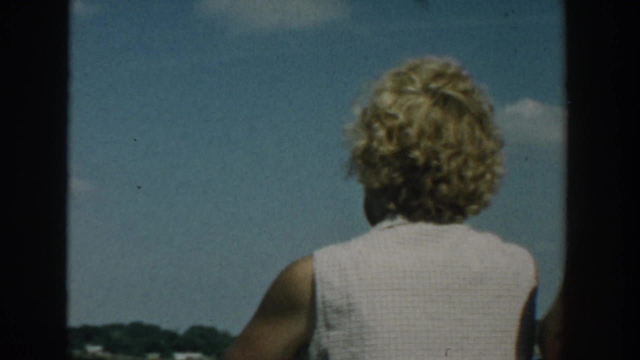 1957 Wisconsin home-movie frame of a woman with curly blonde hair looking outward from a boat toward water and sky.
