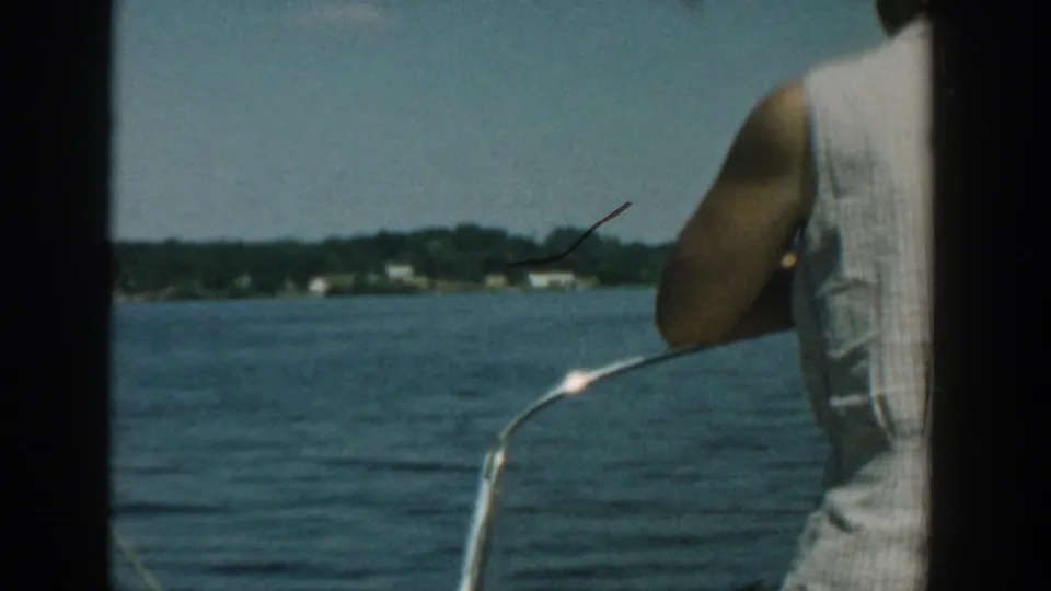 1957 Wisconsin 8mm frame with open water, distant shoreline, boat rail, and a partially visible adult at the right edge.