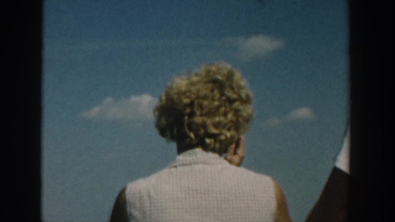 Blonde woman seen from behind against a blue sky with 8mm frame edges.