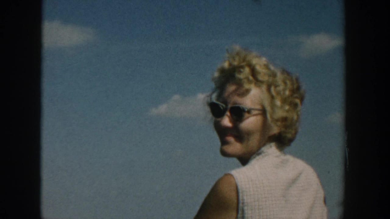 Blonde woman in sunglasses turns and smiles against the blue sky.